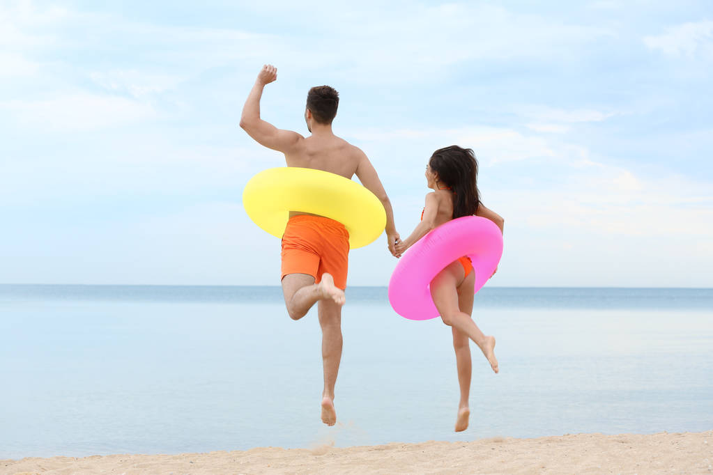Heureux jeune couple s'amuser avec des anneaux gonflables sur la plage près de la mer
 - Photo, image