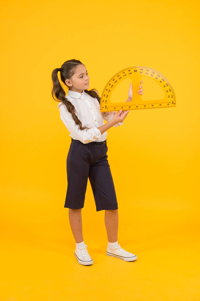 Ρύθμιση τετράγωνο με μοιρογνωμόνιο. Μικρό κορίτσι που χρησιμοποιεί τρίγωνο για να μετρήσει γωνίες σε μοίρες σε κίτρινο φόντο. Μικρό παιδικό μοιρογνωμόνιο για μάθημα γεωμετρίας. Μαθαίνοντας να χρησιμοποιούν μοιρογνωμόνιο - Φωτογραφία, εικόνα