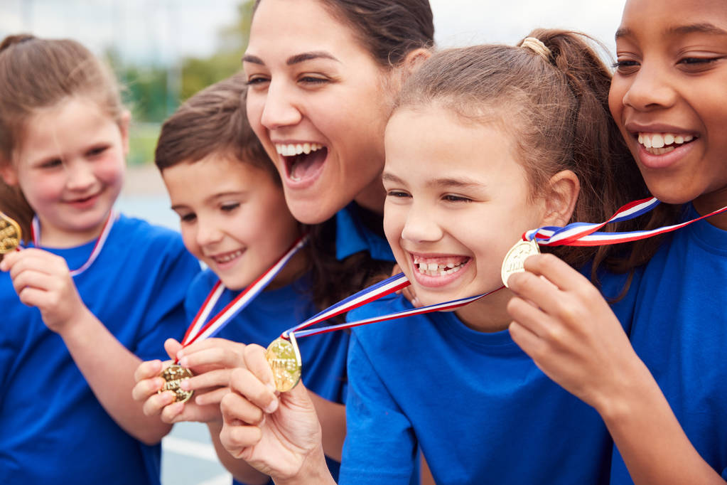 Niños con entrenador femenino mostrando medallas ganadoras en el día del deporte
 - Foto, Imagen