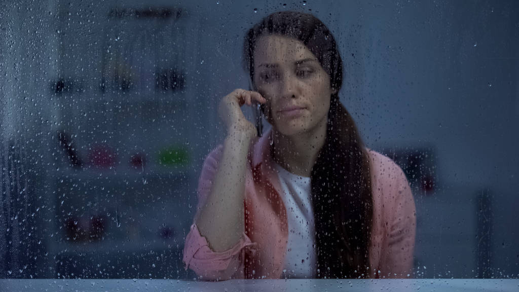 Molesto señora de mediana edad hablando teléfono detrás de la ventana lluviosa, malas noticias, conversación
 - Foto, imagen