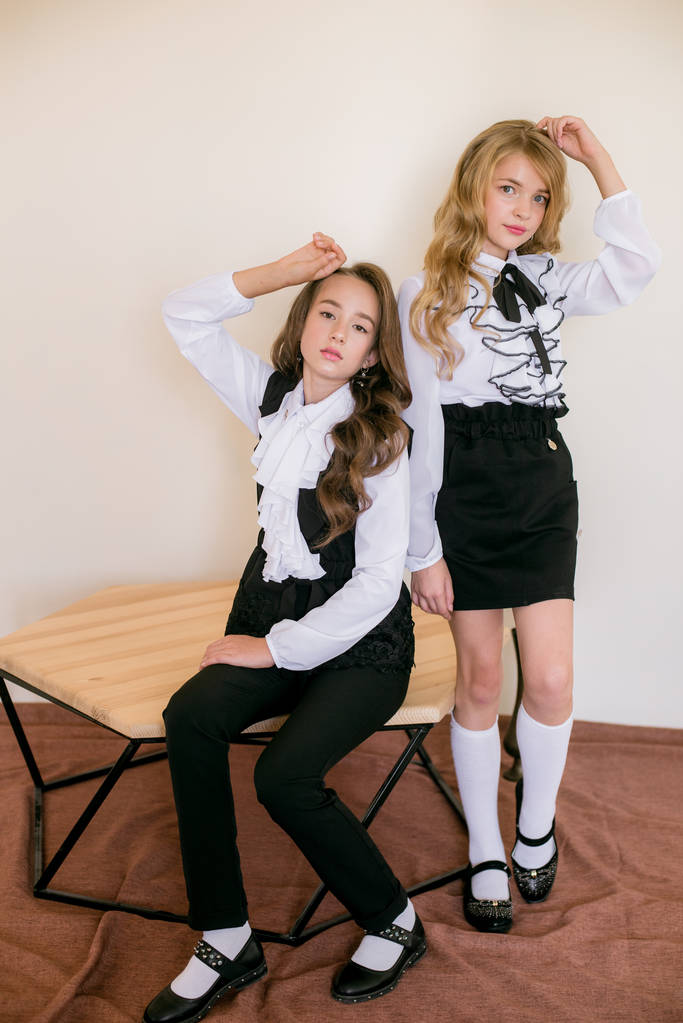 Δύο χαριτωμένα κορίτσια μαθήτριες με μακριά σγουρά μαλλιά σε μοντέρνα σχολικά ρούχα. Σχολική μόδα σε vintage ελίτ στυλ. - Φωτογραφία, εικόνα