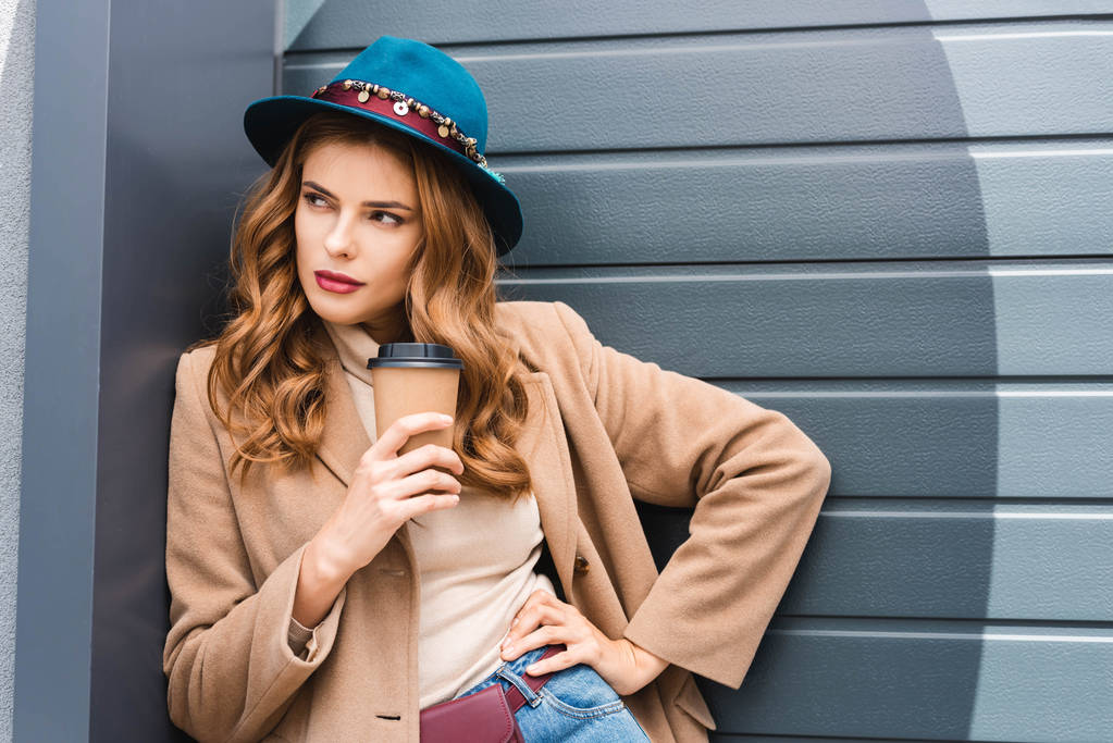 привлекательная женщина в синей шляпе смотрит в сторону и держит бумажную чашку
  - Фото, изображение