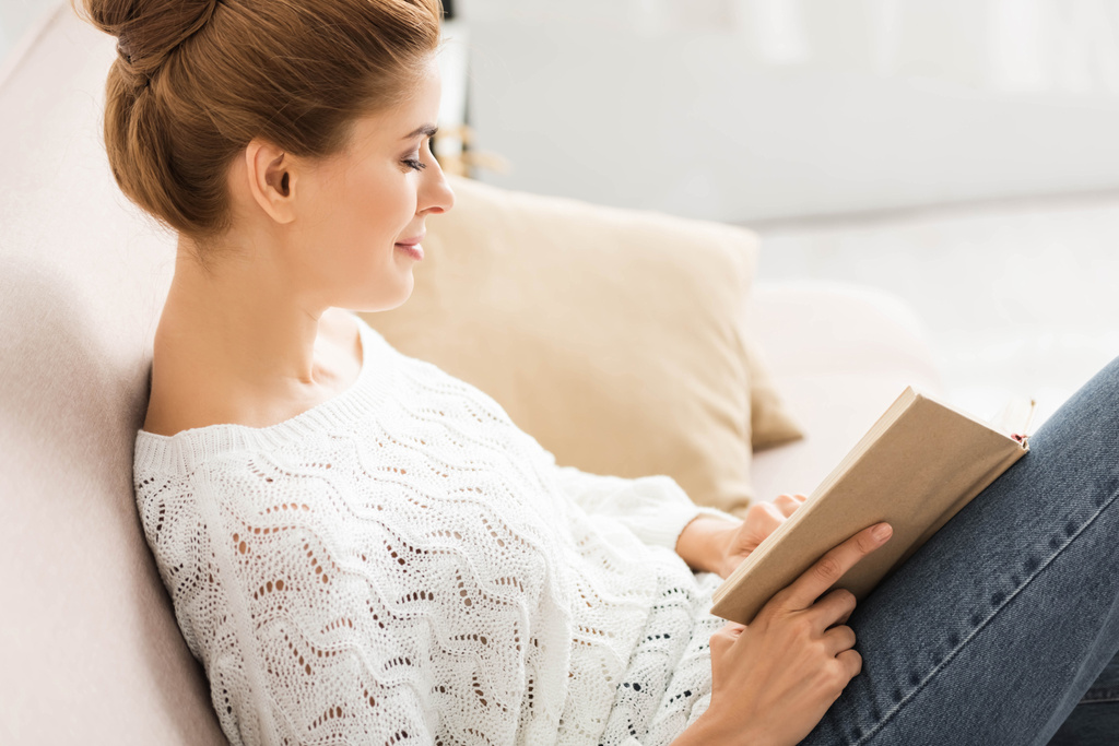 Widok z boku atrakcyjne Kobieta w białym sweter czytanie książki  - Zdjęcie, obraz