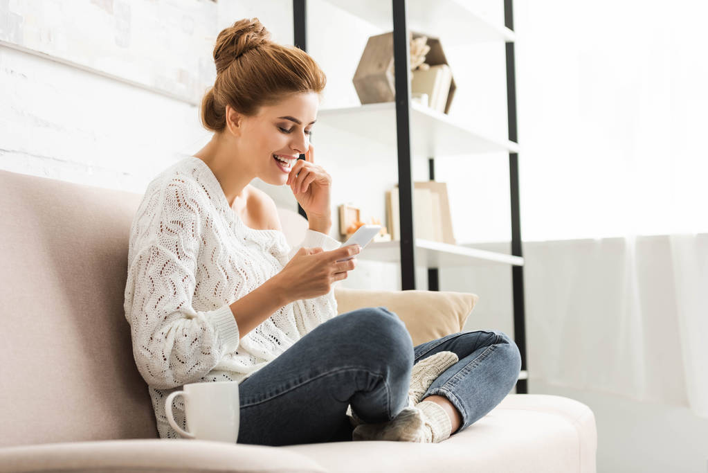 привлекательная женщина в белом свитере улыбается и пользуется смартфоном
  - Фото, изображение