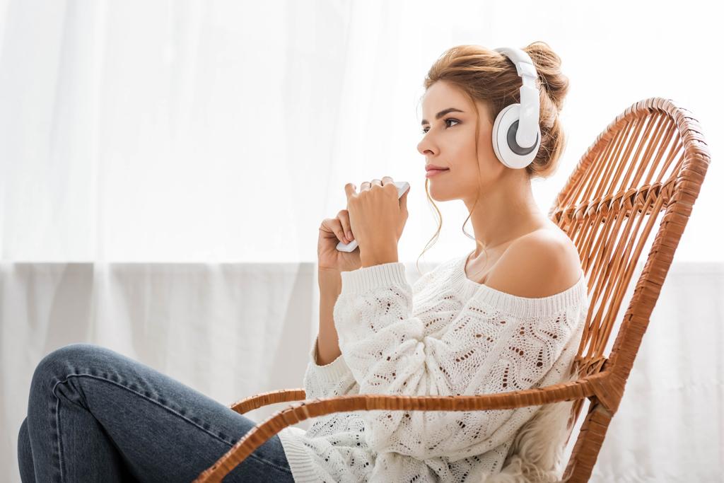 mulher atraente em suéter branco ouvindo música e segurando smartphone
  - Foto, Imagem
