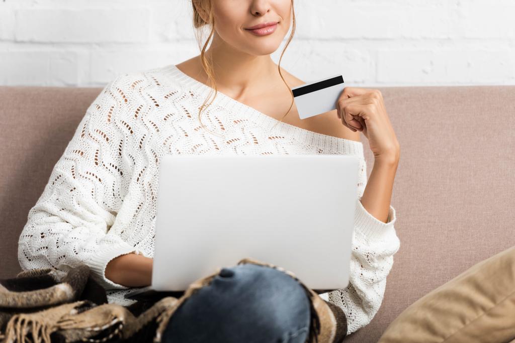 cropped view of woman in white sweater holding credit and laptop - Photo, Image