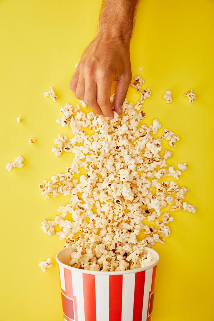 vista ritagliata di uomo prendendo deliziosi popcorn da secchio su sfondo giallo
 - Foto, immagini