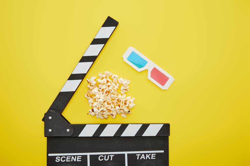 Draufsicht auf knuspriges Popcorn in der Nähe von Klappbrett und 3D-Brille auf gelbem Hintergrund - Foto, Bild