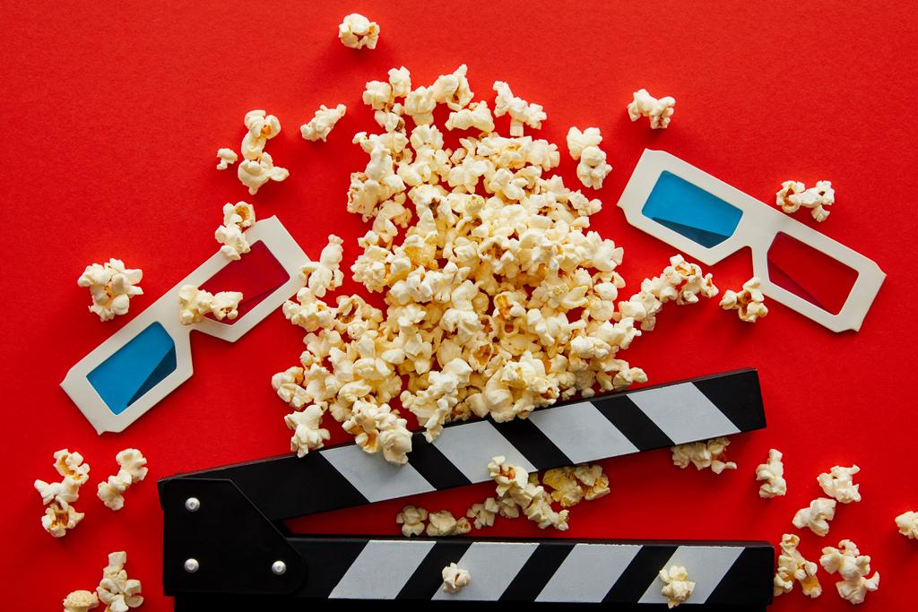 top view of delicious popcorn near clapper board and 3d glasses on red background - Photo, Image