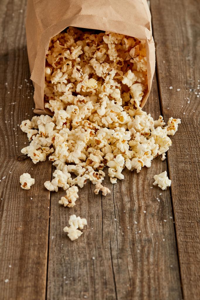 lahodný popcorn rozházený z papírového sáčku na dřevěné pozadí s prostorem pro kopírování - Fotografie, Obrázek