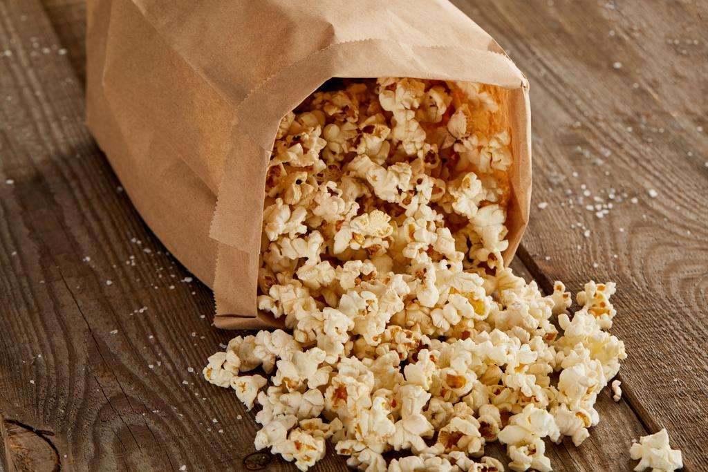 delicious popcorn scattered from paper bag on wooden background - Photo, Image