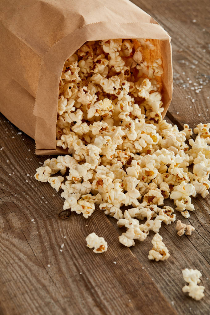 deliziosi popcorn salati sparsi dal sacchetto di carta sulla superficie di legno
 - Foto, immagini