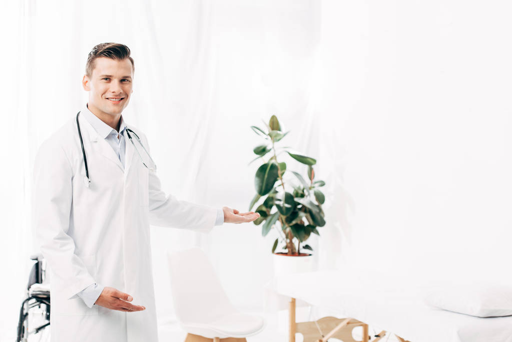 usměvavý doktor v bílém plášti se stetoskem na klinice - Fotografie, Obrázek