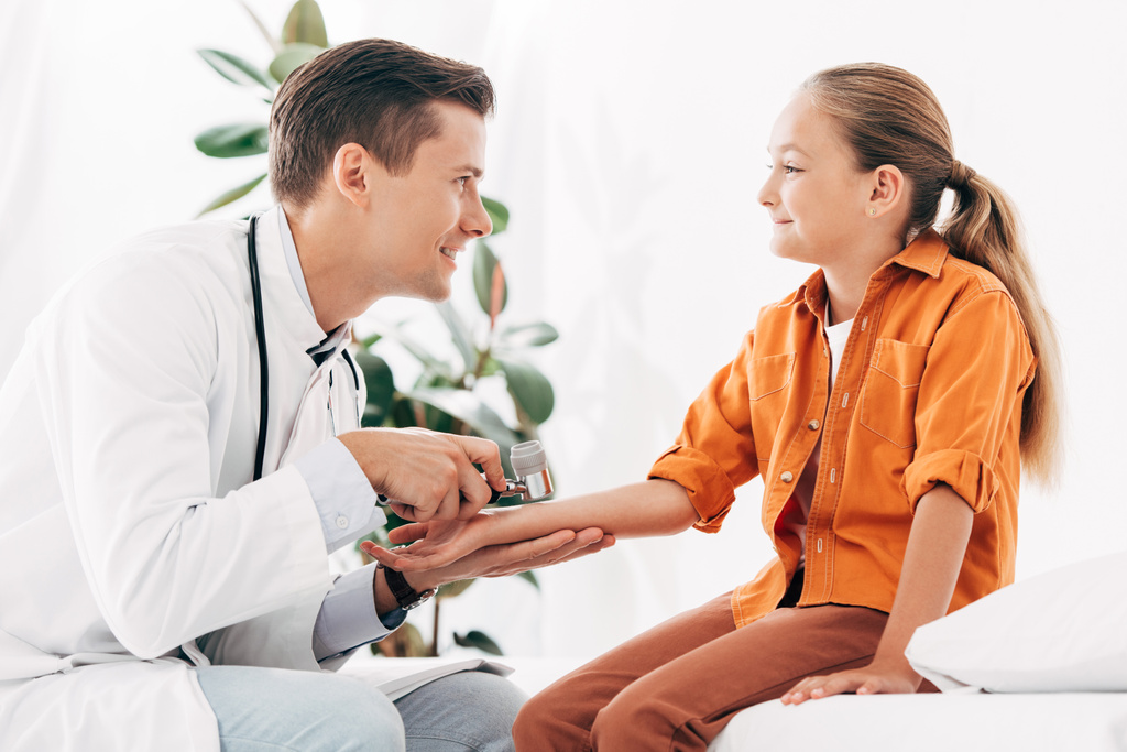 pediatra sorridente in mantello bianco esaminando bambino con dermascopio
 - Foto, immagini