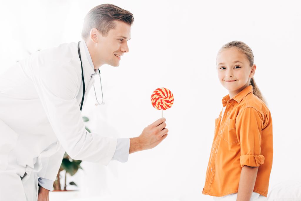 pediatra de bata blanca dando caramelos a los niños en la clínica
 - Foto, Imagen