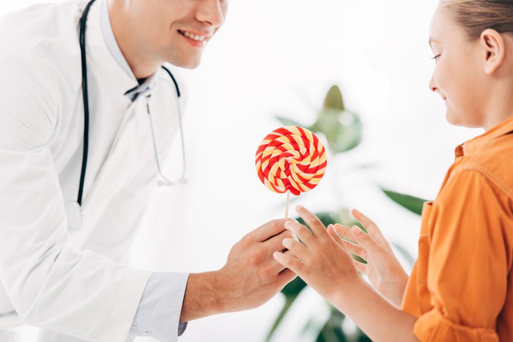 vue partielle du pédiatre en manteau blanc donnant des bonbons à l'enfant à la clinique
 - Photo, image