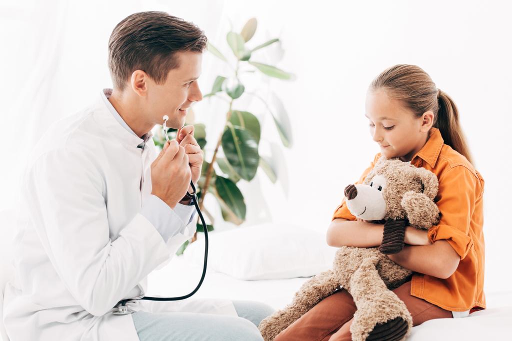 pediatra sorridente in cappotto bianco e bambino con orsacchiotto in clinica
 - Foto, immagini