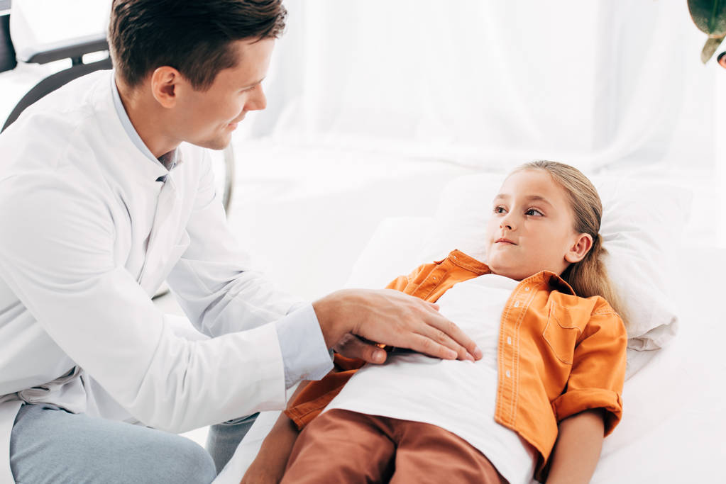 uśmiechnięty rodak w białej sierści badający dziecko w klinice - Zdjęcie, obraz