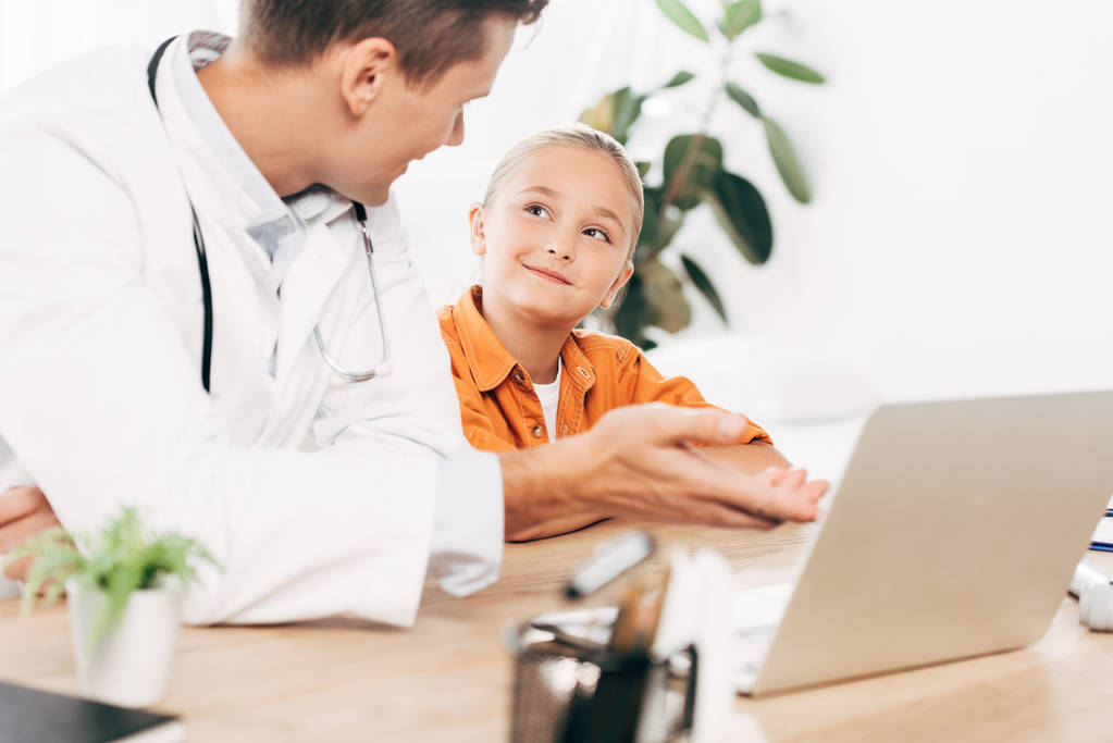 pediatra in cappotto bianco e bambino con computer portatile in clinica
 - Foto, immagini