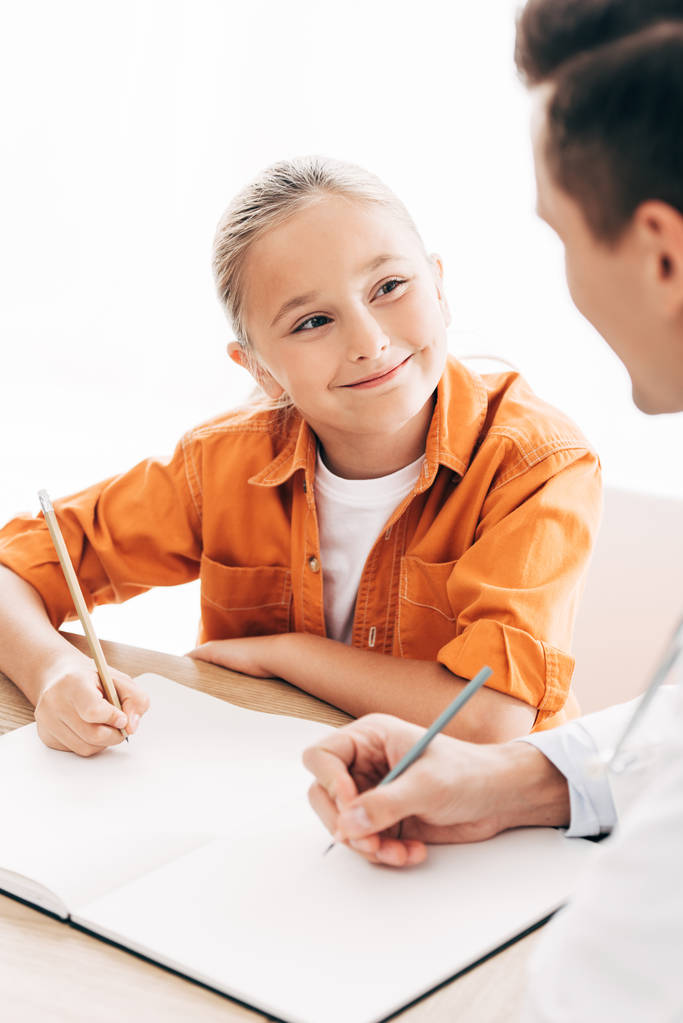 hymyilevä lapsi ja lastenlääkäri kirjoittaminen muistikirjaan pöydässä klinikalla
 - Valokuva, kuva