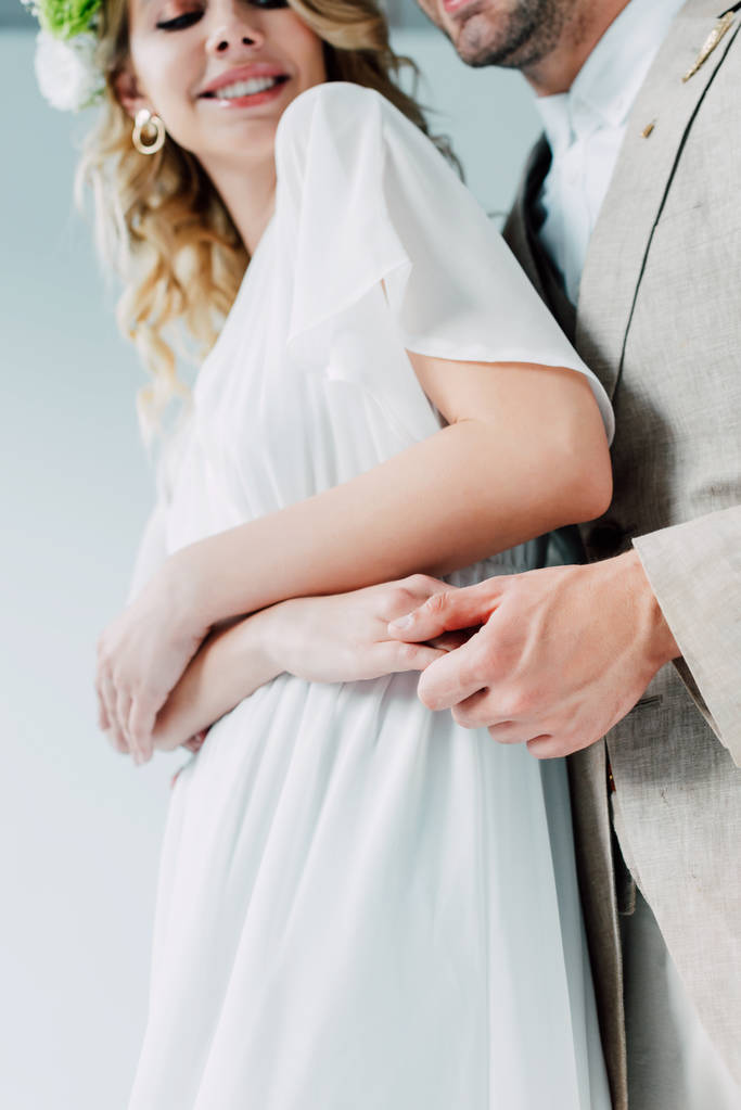 vista recortada de la novia y el novio sonriendo y tomándose de las manos aisladas en gris
 - Foto, Imagen