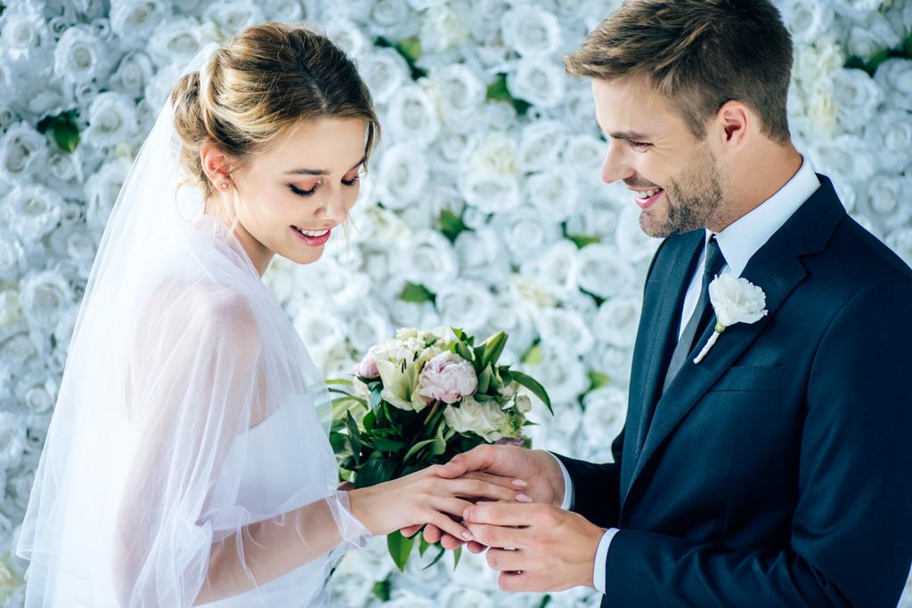 guapo y sonriente novio poniendo anillo de bodas en el dedo
  - Foto, imagen