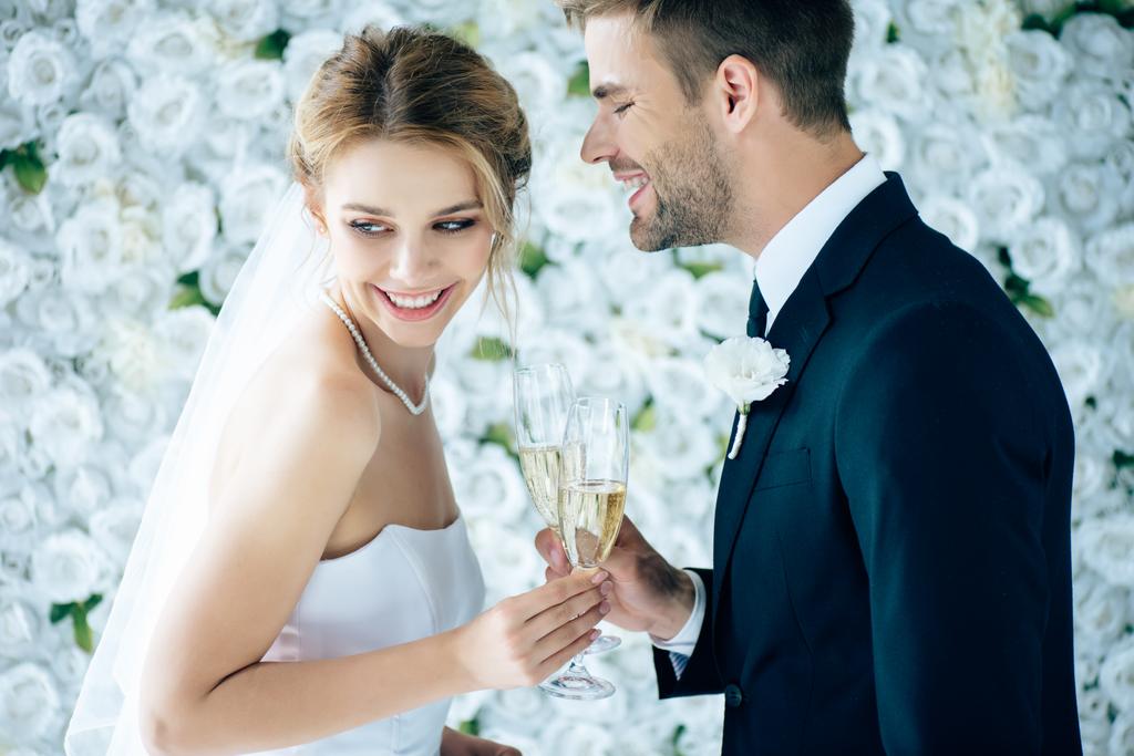 aantrekkelijke bruid en knappe bruidegom glimlachen en geproost met Champagne glazen - Foto, afbeelding