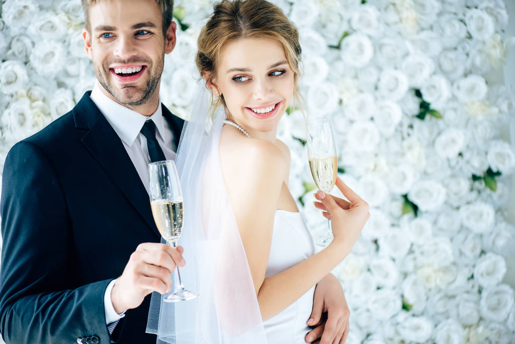 attractive bride and handsome bridegroom smiling and holding champagne glasses - Photo, Image