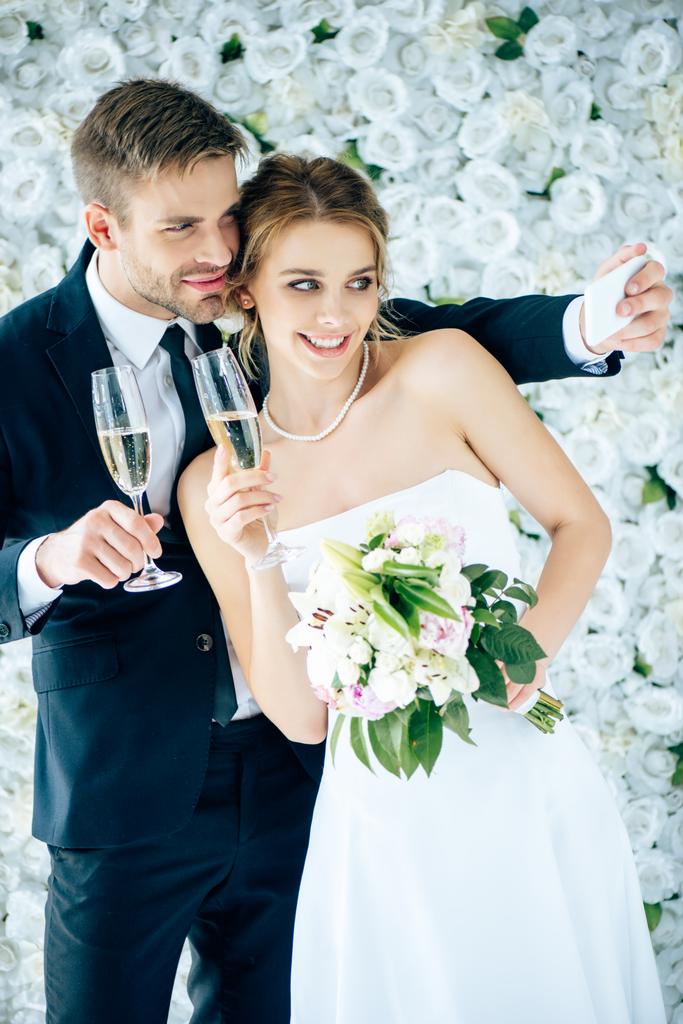 ελκυστική νύφη και όμορφος γαμπρός χαμογελώντας και παίρνοντας selfie  - Φωτογραφία, εικόνα