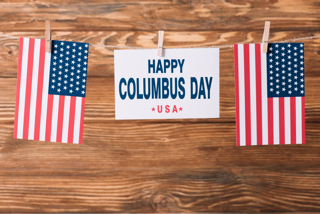 card with happy Columbus day inscription between American national flags on wooden surface - Photo, Image