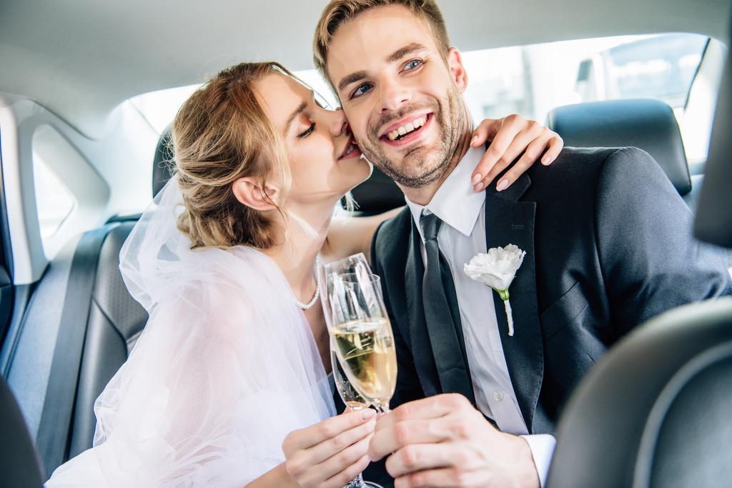 ελκυστική νύφη και όμορφος γαμπρός φιλιά και κουδουνιά με ποτήρια σαμπάνιας - Φωτογραφία, εικόνα