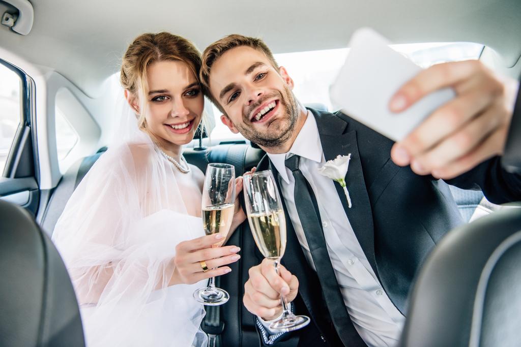 attractive bride and handsome bridegroom taking selfie in car  - Photo, Image