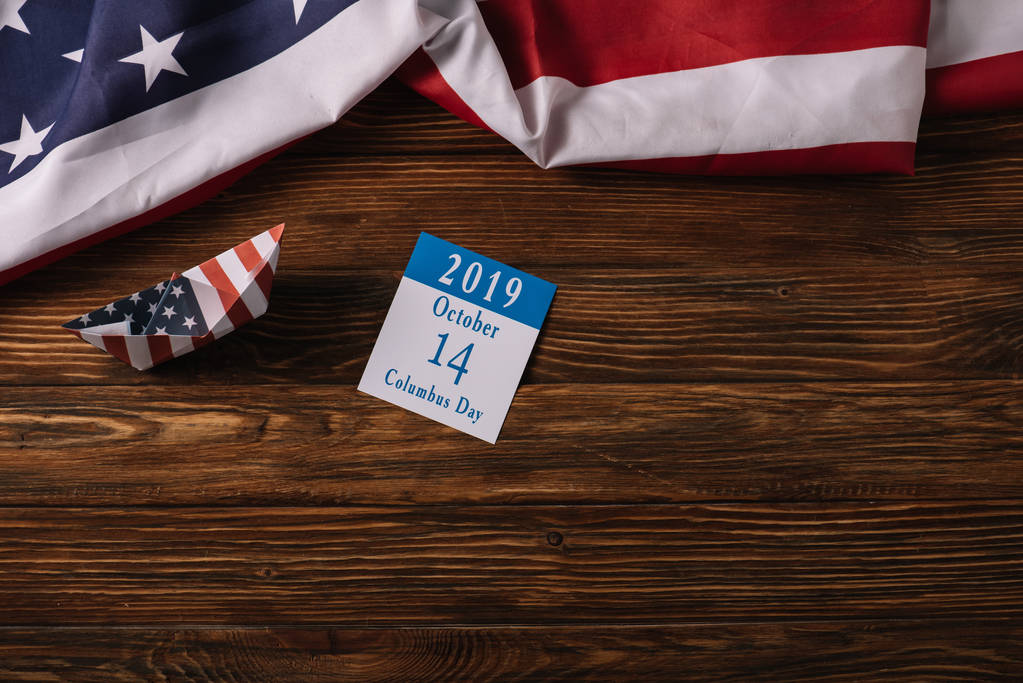 vista dall'alto del calendario con iscrizione Columbus Day e barca di carta su superficie di legno con bandiera nazionale americana
 - Foto, immagini