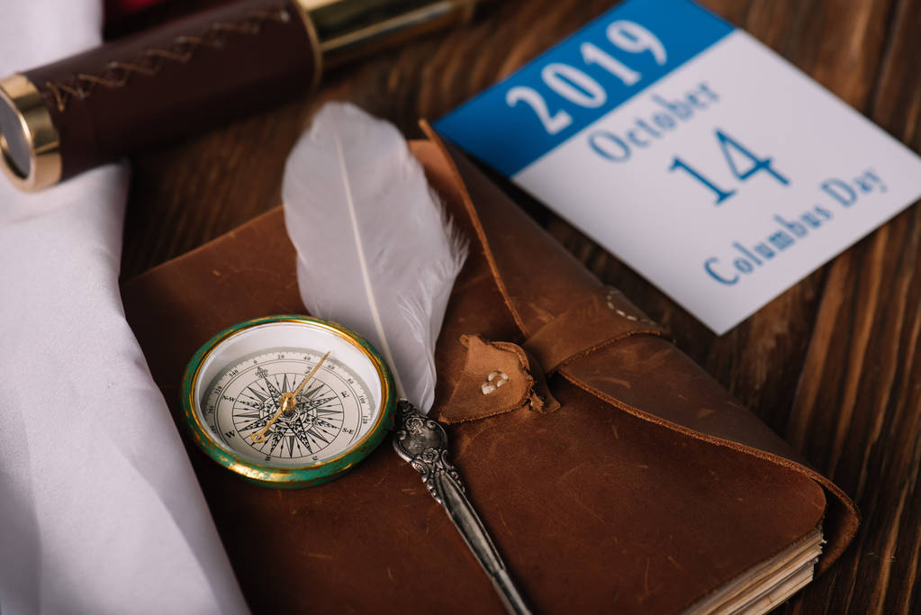 Kalendarz z datą 14 października w pobliżu skórzanego notebooka ze stalówką i kompasem na drewnianej powierzchni - Zdjęcie, obraz