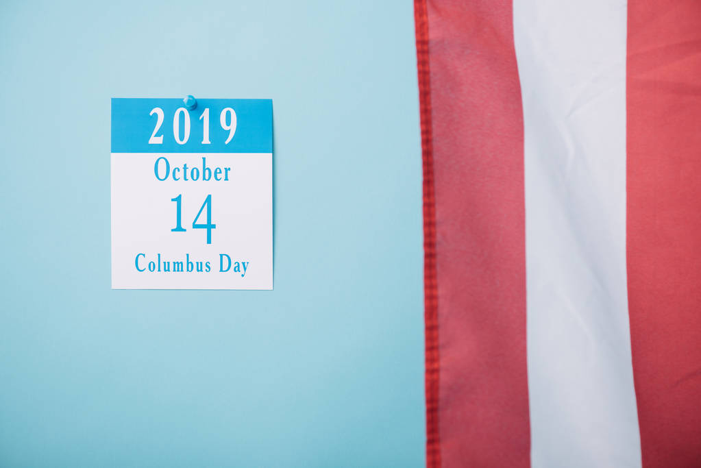 Kalendarz papierowy z napisem Columbus Day w pobliżu części amerykańskiej flagi narodowej na niebieskim tle - Zdjęcie, obraz