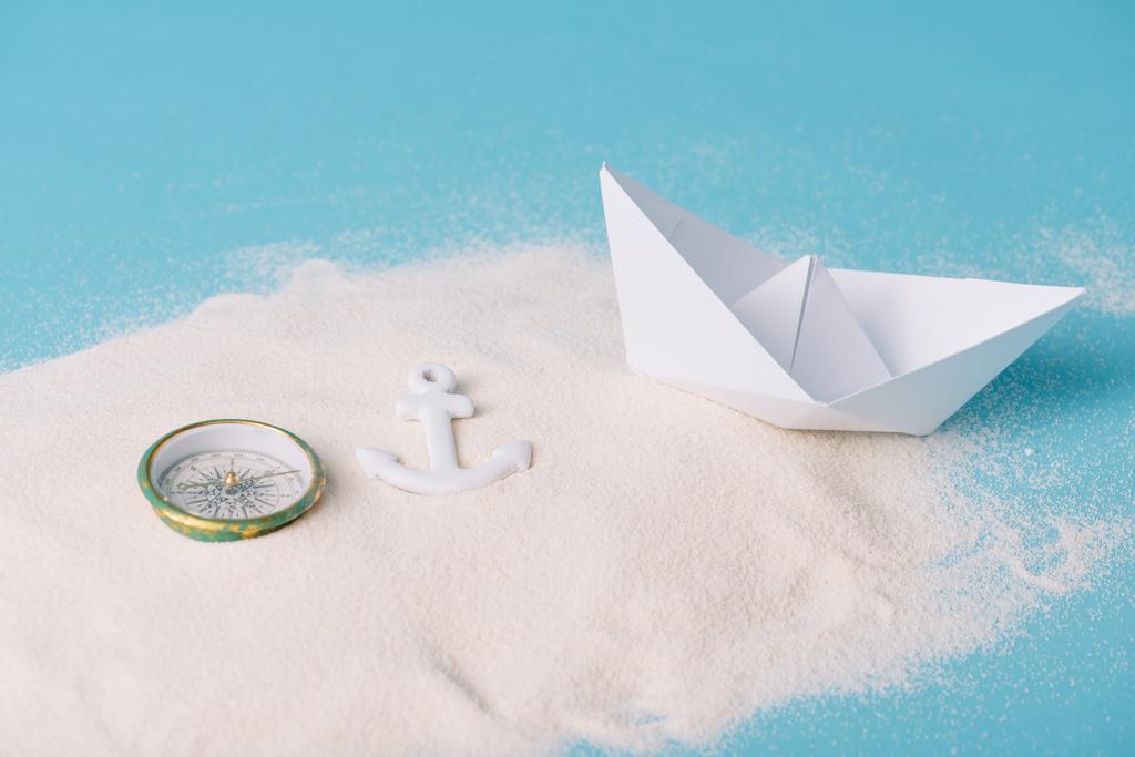areia com barco de papel, bússola e âncora no fundo azul
 - Foto, Imagem