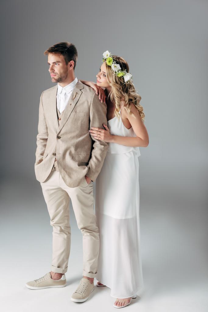 ウェディングドレスとスーツでハンサムな花婿を抱きしめる花輪の花嫁  - 写真・画像