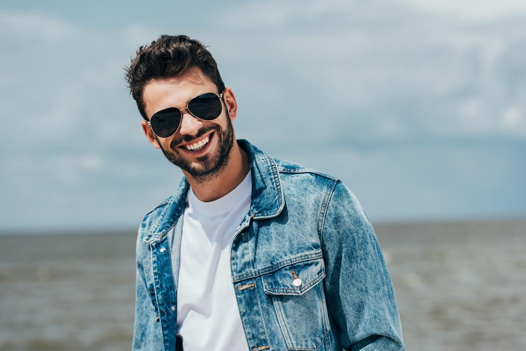 handsome man in denim jacket and sunglasses looking at camera  - Photo, Image