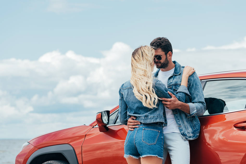 blonde Frau und schöner Mann in Jeansjacken umarmen sich draußen  - Foto, Bild