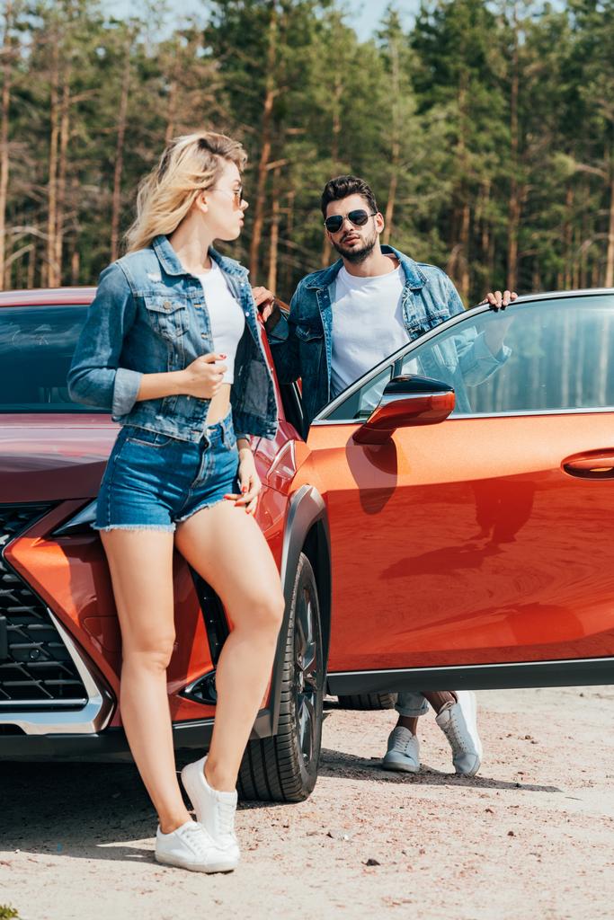 atrakcyjna kobieta i przystojny mężczyzna w kurtki stojące w pobliżu samochodu - Zdjęcie, obraz