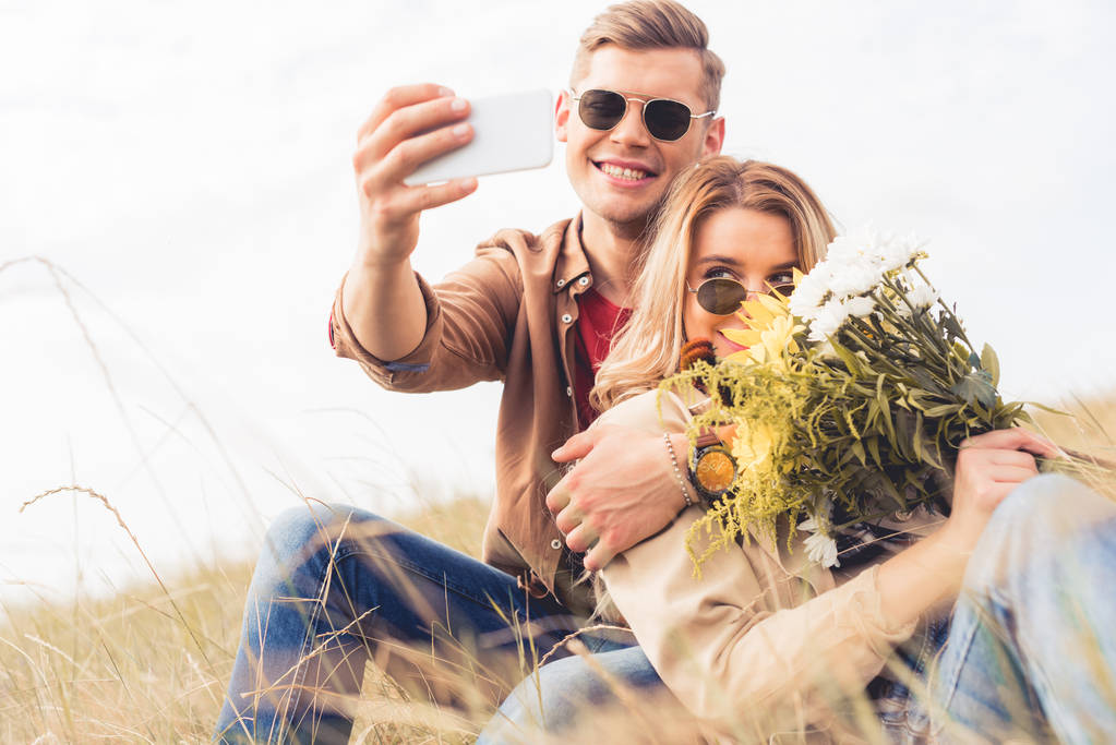 attraktive Frau mit Blumenstrauß und schöner Mann, der ein Selfie macht  - Foto, Bild