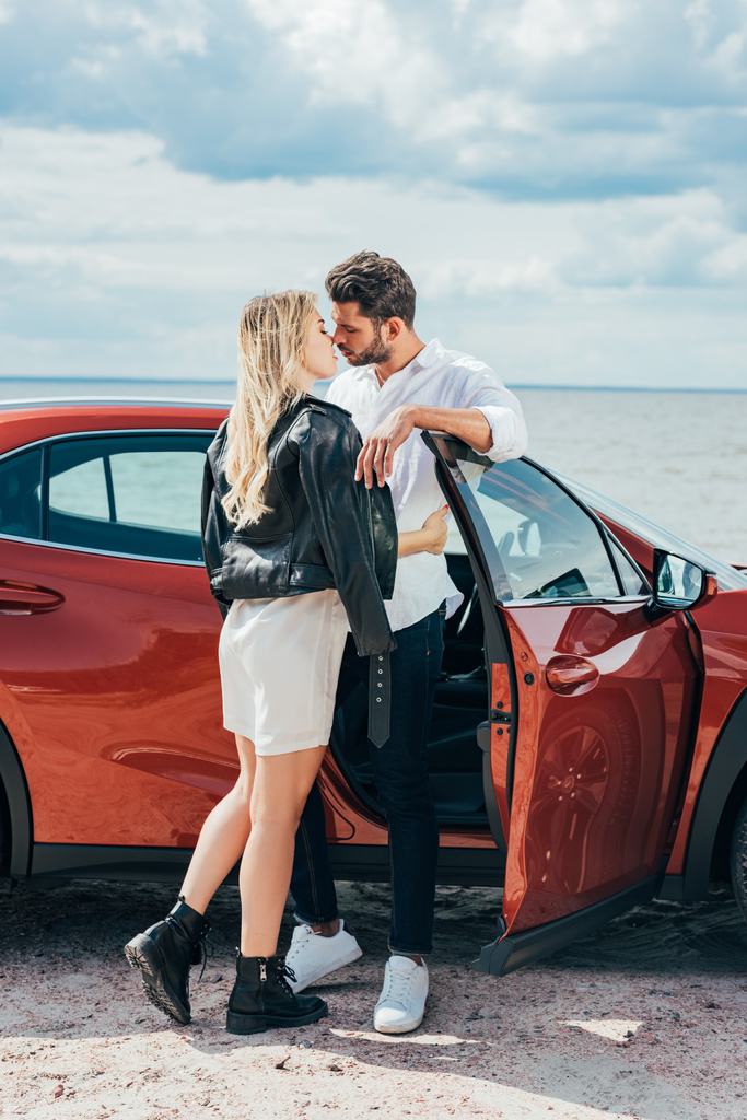 魅力的な女性とハンサムな男性が車の近くでキスして抱きしめる  - 写真・画像