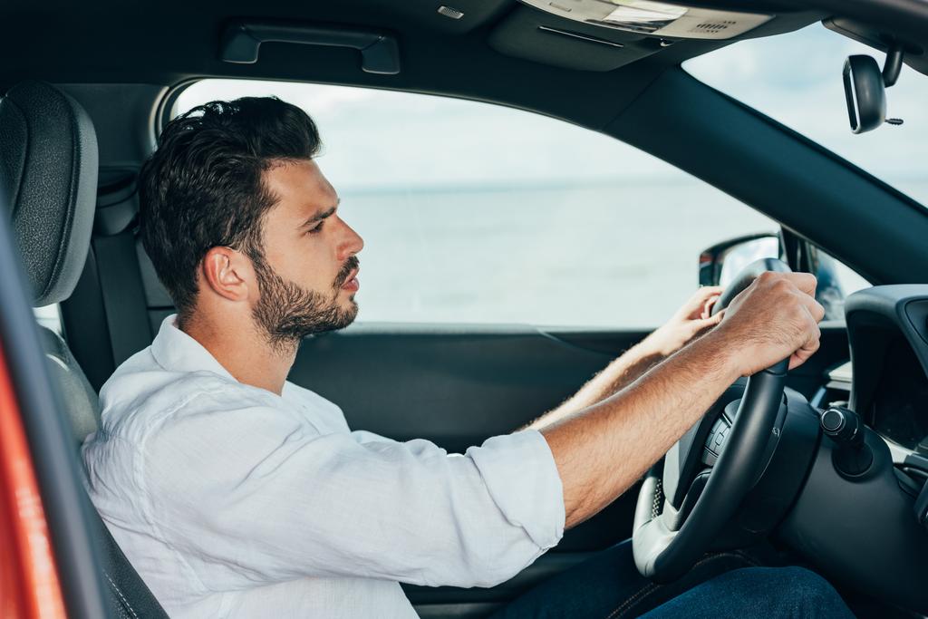 beyaz gömlekli yakışıklı adam araba sürüyor ve uzağa bakıyor  - Fotoğraf, Görsel
