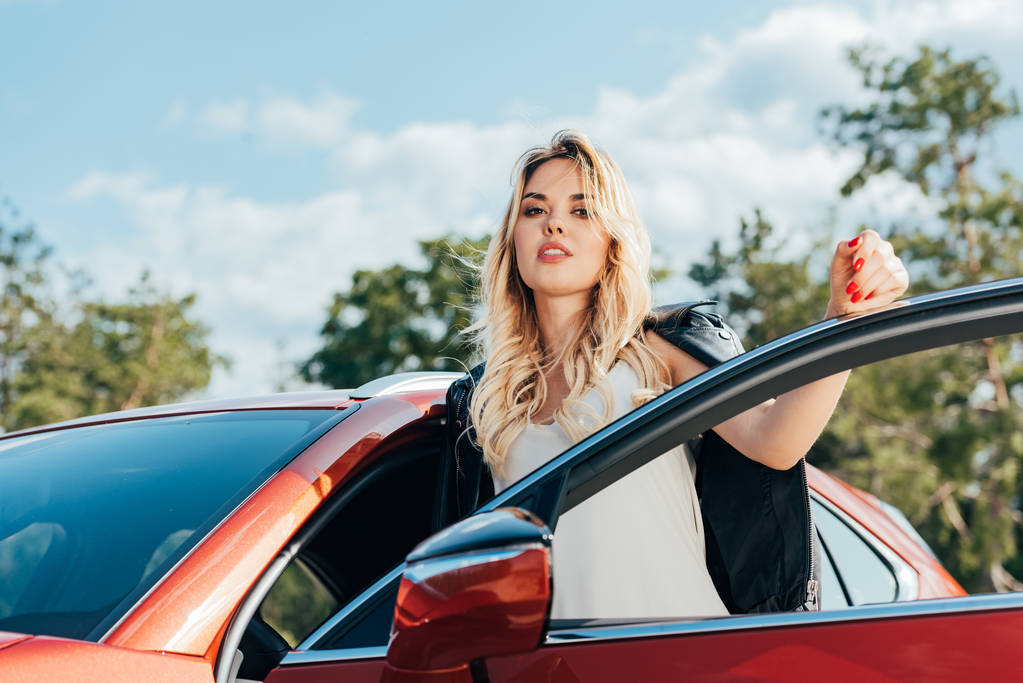 Atrakcyjna i blond kobieta stoi w pobliżu samochodu i patrząc na kamerę  - Zdjęcie, obraz
