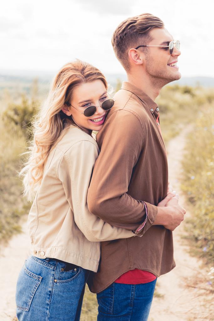 привлекательная и улыбающаяся женщина обнимает красивого мужчину в солнечных очках
 - Фото, изображение