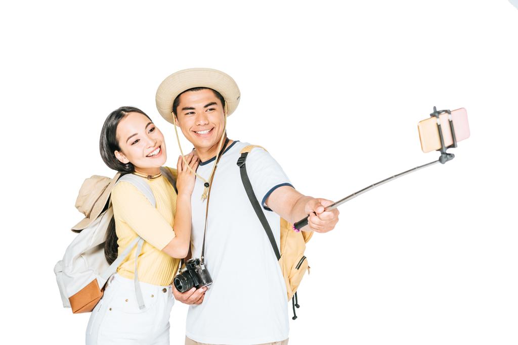 zwei glückliche asiatische Touristen machen Selfie auf dem Smartphone mit Selfie-Stick isoliert auf weiß - Foto, Bild