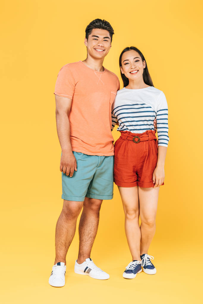 黄色の背景にカメラを見て夏服で陽気なアジアのカップル - 写真・画像