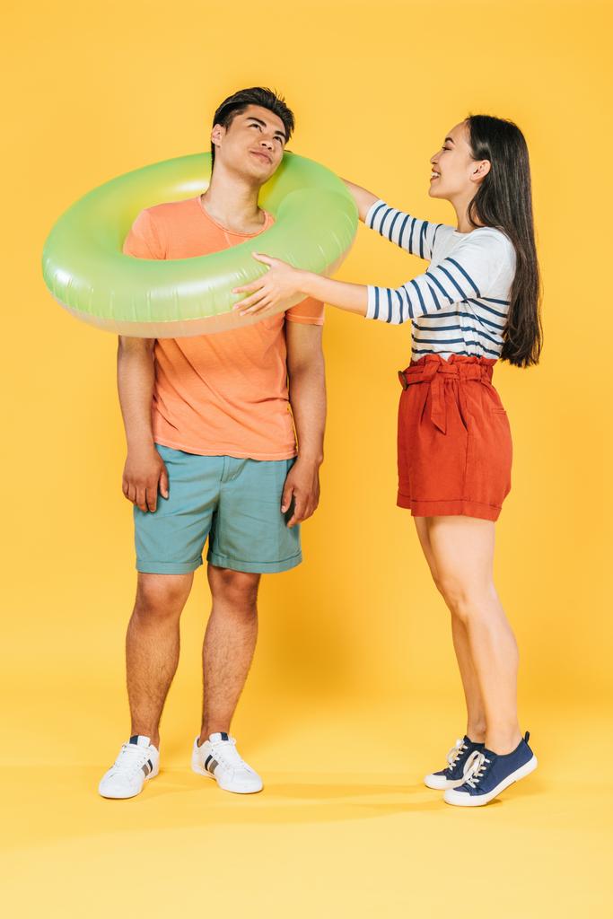happy asian girl putting swim ring on smiling boyfriend on yellow background - Photo, Image