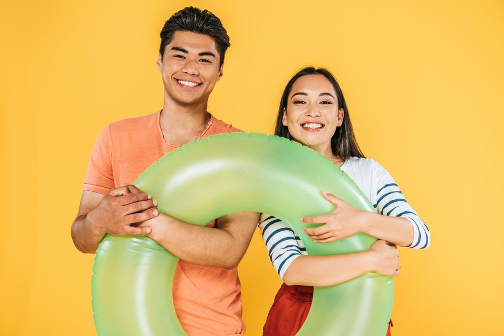 happy asian man and woman holding swim ring and smiling at camera isolated on yellow - Photo, Image
