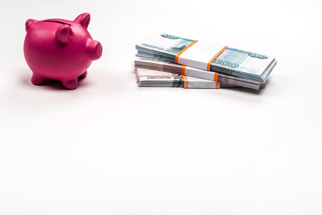 ροζ κουμπαράς κοντά σε στοίβες από Ρωσικά χρήματα σε λευκό  - Φωτογραφία, εικόνα